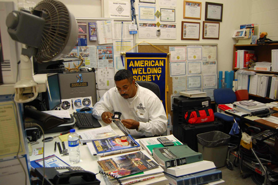 Jenord Alston works at his desk, surrounded by books and papers on welding