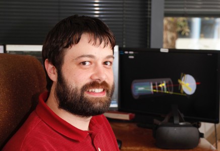 Thomas Britton in his office, in front of a computer displaying a 3D wire frame of the GlueX detector