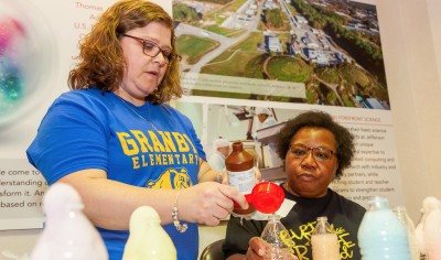 Teachers pour red liquid into a beaker for a science demo